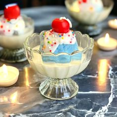 three desserts in glass dishes on a table with lit candles around the bowl and one has a cherry on top