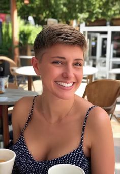 "A playful pixie cut on a woman with a confident smile, enjoying a sunny summer day. She’s outdoors at a café, with natural sunlight highlighting the sharp angles and texture of her pixie cut hairstyle." Natural Sunlight, Pixie Haircut, Pixie Cut, Summer Days, Hair Cuts