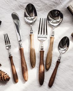 six forks, knives and spoons are laid out on a white tablecloth with pine cones