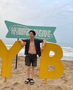 a man standing in front of a big sign on the beach with his shirt off