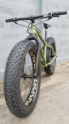 a green bike parked in front of a gray brick building with no wheels on it