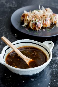 a bowl of soup next to a plate of food on a black counter top with a wooden spoon in it