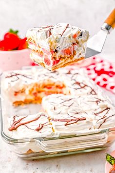 a piece of cake is being lifted by a knife from a glass dish with strawberries in the background