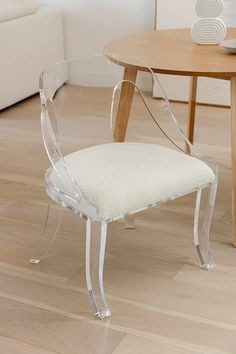 a clear chair sitting on top of a hard wood floor next to a white couch