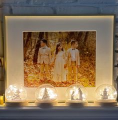 three children are standing in front of a photo on a mantle with snow globes