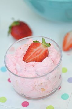 a bowl filled with strawberry fluff next to two strawberries on a polka dot tablecloth