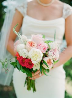 a bride holding a bouquet of pink and white flowers on her wedding day in front of a brick wall