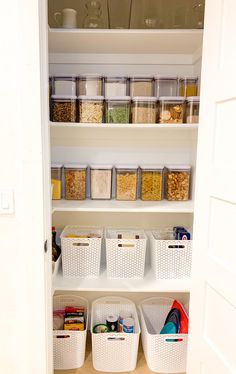 an organized pantry with white bins and plastic baskets on the bottom shelf, full of food