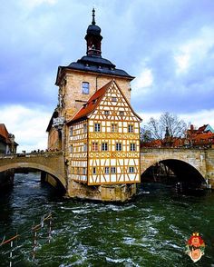 an old building sitting on the side of a river with a bridge in the background