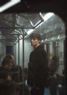 a man standing in front of a mirror on a subway train with other people behind him