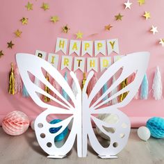 a white butterfly cutout sitting on top of a table next to balloons and streamers