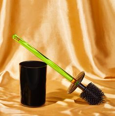 a black cup with a green handle next to a brush on a gold cloth background