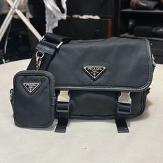 Prada Re-Nylon And Saffiano Leather Shoulder Bag Unisex Also Posted Hat Separately M Nice Conversation/ Status Piece Great Bag, Preserved Very Well Reduced Price Due To Minor Flaws Comes With Box Taking Offers - Small Pouch Zipper Fading( No One Pays It Any Attention)As Shown In Pic. I Had Small Pouch Hook Strap Reinforced To Keep From Tearing Away From The Leather( Also Unnoticed)As Shown In Pic Waiting For A New Home Designer Black Shoulder Bag With Silver-tone Logo, Designer Black Bag With Silver-tone Logo Plaque, Designer Black Bag With Silver-tone Logo, Small Pouch, Small Pouches, Zipper Pouch, Leather Shoulder Bag, New Home, Prada