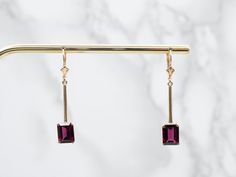 These garnet drop earrings create an elegant line along the neck! Sleek gold bars catch the light and lead the eye to the garnets set at the base. These sophisticated gemstones have a deep red hue that sparkles with bright flashes of crimson.Metal: 14K Yellow GoldGem: 2 Garnets totaling 5.53 CaratsGem Measurements: 7.1 x 9.2 mm, Emerald CutEarrings Length: 41.2 mmEarrings Width: 7.1 mmMarks: "(C)P8014K" Stamped on the reverse Elegant Burgundy Earrings For Formal Occasions, Elegant Yellow Gold Garnet Earrings, Elegant Burgundy Jewelry For Formal Occasions, Classic Burgundy Jewelry For Formal Occasions, Classic Formal Burgundy Jewelry, Garnet Drop Earrings, Gold Bars, Retro Era, Filigree Pendant