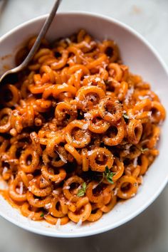 a white bowl filled with pasta and sauce on top of a table next to a spoon