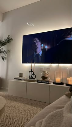 a flat screen tv mounted to the side of a wall next to a table with candles on it