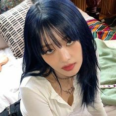 a woman with black hair and bangs sitting on a bed