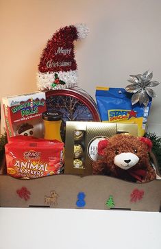 a teddy bear sitting in a box filled with snacks and candys next to a christmas tree