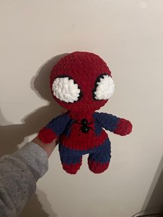 a hand holding up a crocheted spiderman stuffed animal