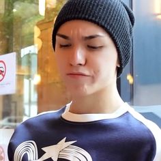 a young man wearing a beanie looks at his cell phone in front of a store window