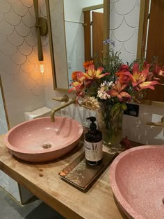 two pink bathroom sinks sitting next to each other on a wooden table with flowers in the vase