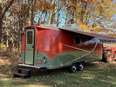 an orange and green trailer parked in front of some trees with leaves on the ground