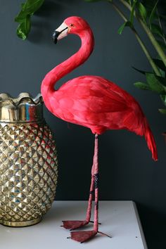 a pink flamingo standing next to a gold vase