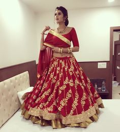 a woman in a red and gold lehenga is standing on a bed with her hands behind her head