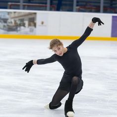 a woman skating on an ice rink wearing black clothing and holding her arms in the air