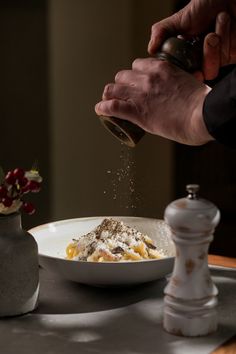 a person is sprinkling sugar on food in a white bowl next to a vase