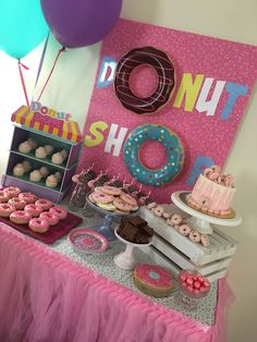 a table topped with lots of donuts next to a pink sign and some balloons