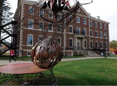 a metal sculpture sitting on top of a wooden bench in front of a brick building