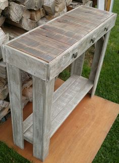 a wooden table sitting in the grass next to stacks of firewood and wood logs