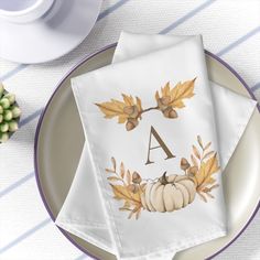 two napkins on a plate with a monogrammed initial and autumn leaves in the middle