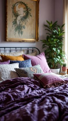 a bed with purple sheets and pillows in front of a painting hanging on the wall