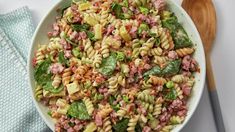 a white bowl filled with pasta salad next to a green napkin and wooden spoons