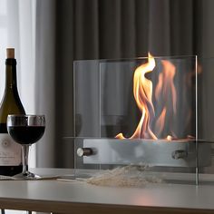 a bottle of wine sitting next to a fire place with a glass on the table