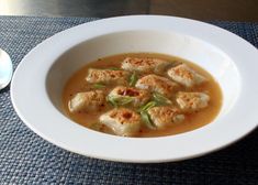 a white bowl filled with soup on top of a blue place mat next to a spoon