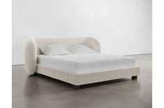 a bed that is made up with white sheets and pillows on it's headboard