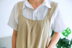 a woman standing in front of a plant wearing a white shirt and tan overalls