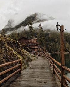 a wooden bridge over a body of water with mountains in the background and foggy sky