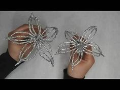 two silver flowers are being held up by someone's hands on a white surface