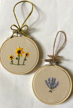 two cross stitch flowers are hanging from twine hoops on a white tablecloth