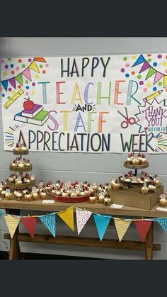 a table with cupcakes on it in front of a happy teacher and staff sign