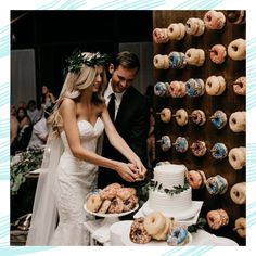 a bride and groom cutting their wedding cake at the reception table with doughnuts on the wall behind them