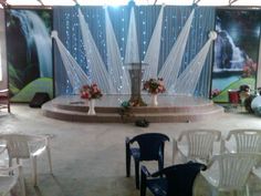 a stage set up with white chairs and flowers in the center, surrounded by curtained walls