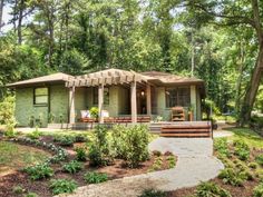 a small green house surrounded by trees in the middle of a wooded area with steps leading up to it's front door