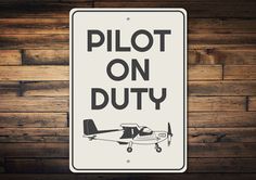 a sign that says pilot on duty against a wooden wall with planks in the background