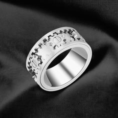 a silver ring with gears on it sitting on a black cloth in front of a black background