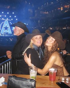 two women and one man wearing cowboy hats at a bar